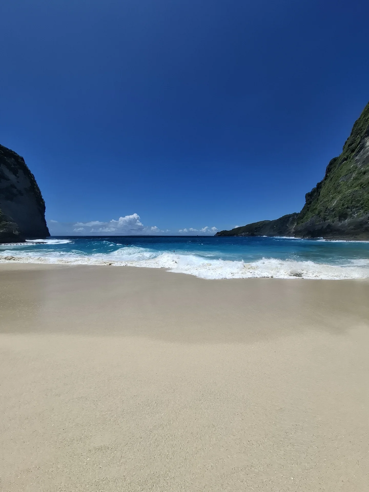 A bright blue sea meeting a quiet stretch of pale sand