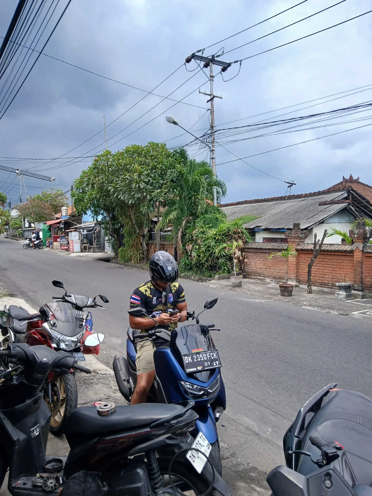 Dainyel standing beside his blue scooter on a Bali street